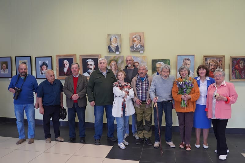 Группа слонимских художников позирует для общей фотографии в выставочном зале на фоне живописных портретов