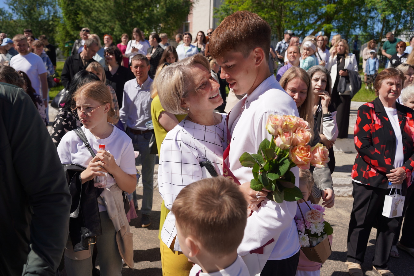 Выпускник с букетом цветов обнимает учительницу на празднике последнего звонка