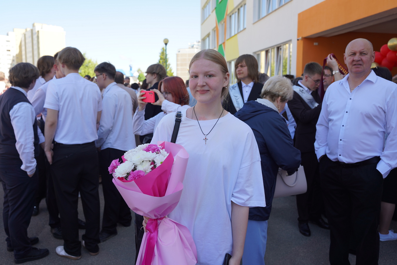 Девушка с букетом цветов стоит у школы во время праздника последнего звонка