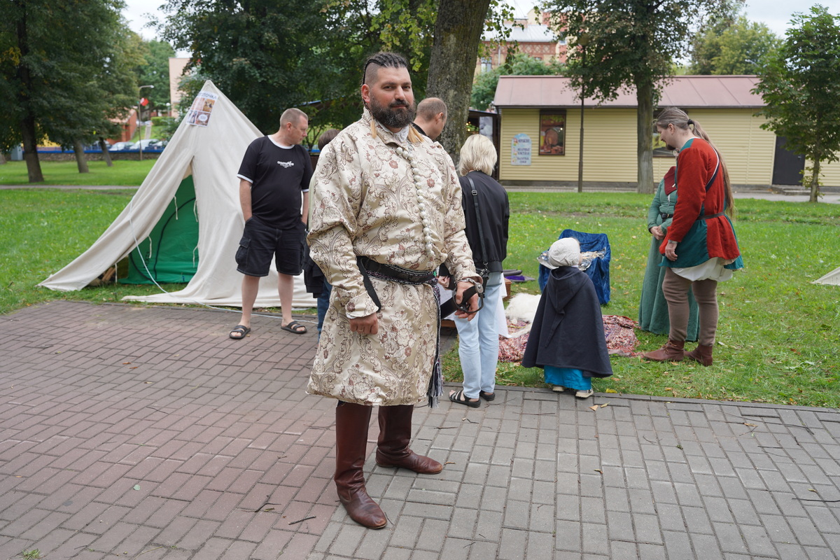 Мужчина в историческом костюме стоит на плитке в парке рядом с палаткой.